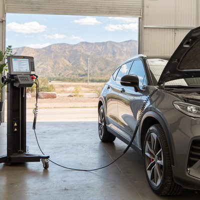A hybrid crossover being inspected inside an independent repair shop with Colorado foothills visible beyond the service bay.